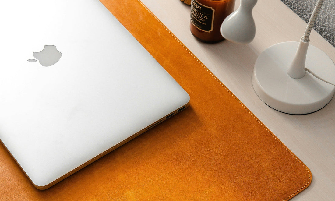 Leather desk pad and Apple devices in warm light illustrating tactile design by HappyPatina