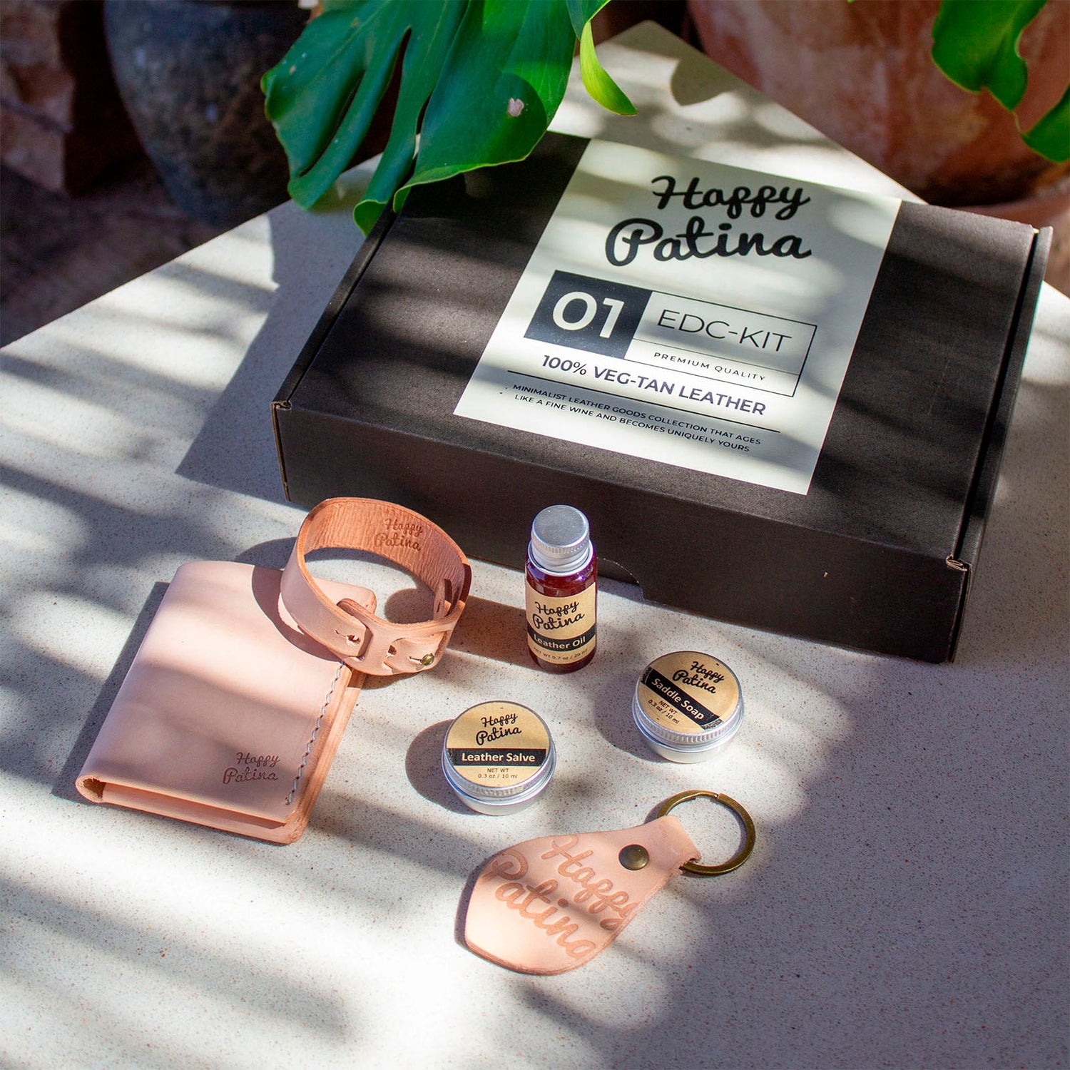 HappyPatina EDC Kit components (wallet, key fob, wristband, leather care) in natural veg-tan leather